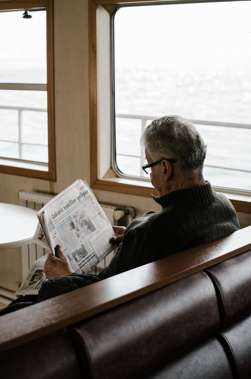 man sitting on bench while reading newspaper